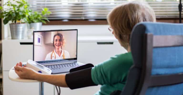 A patient taking their blood pressure during a telemedicine appointment, preparing questions to ask during a sick visit to communicate clearly with their provider.